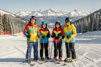 Famille en tenue de ski colorée sur les pistes enneigées de La Plagne avec panorama des Alpes en arrière-plan